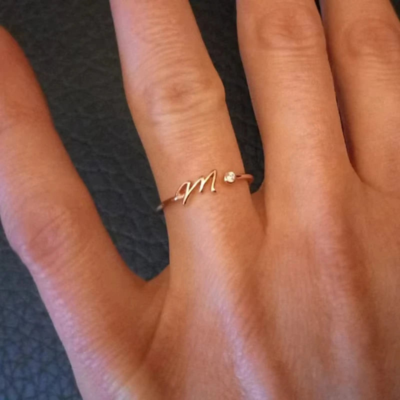 A delicate and elegant Infinity gold ring featuring a minimalist design with a small sparkling diamond accent, worn on a hand against a dark textured background.